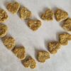 Heart-shaped dog treats, light brown and textured, arranged in a heart shape on a light surface.
