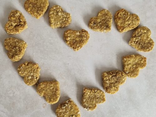 Heart-shaped dog treats, light brown and textured, arranged in a heart shape on a light surface.