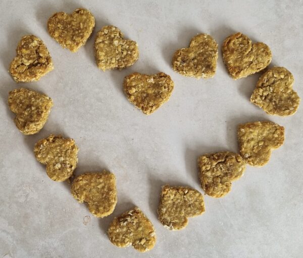 Heart-shaped dog treats, light brown and textured, arranged in a heart shape on a light surface.