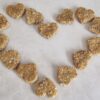 Heart-shaped dog treats, light brown and textured, arranged in a heart shape on a light surface.