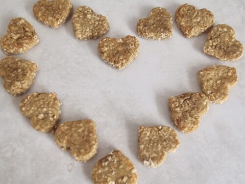 Heart-shaped dog treats, light brown and textured, arranged in a heart shape on a light surface.