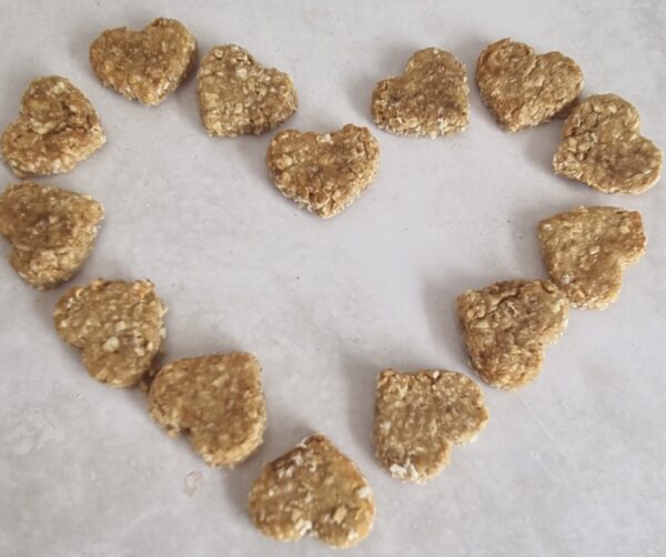 Heart-shaped dog treats, light brown and textured, arranged in a heart shape on a light surface.