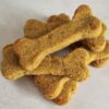A pile of bone-shaped dog treats, golden-brown and textured, stacked on a light surface.
