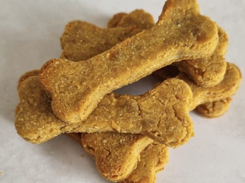 A pile of bone-shaped dog treats, golden-brown and textured, stacked on a light surface.