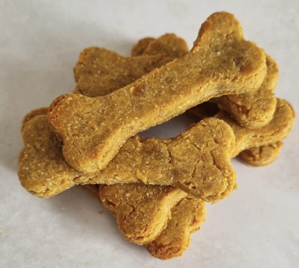 A pile of bone-shaped dog treats, golden-brown and textured, stacked on a light surface.