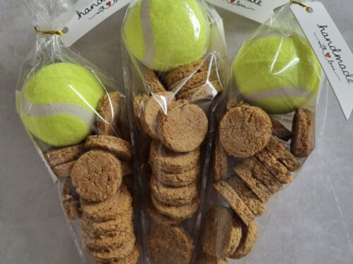 hree clear cellophane bags, each containing a bright yellow tennis ball and a pile of small, round dog treats, with 'handmade with love' tags.