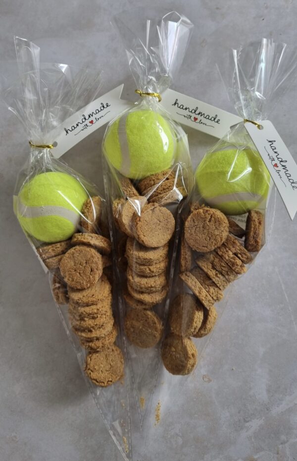 hree clear cellophane bags, each containing a bright yellow tennis ball and a pile of small, round dog treats, with 'handmade with love' tags.