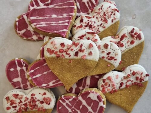 Collection of Love Bites Valentine dog treats UK showing variety of heart-shaped cookies with pink icing and sprinkles